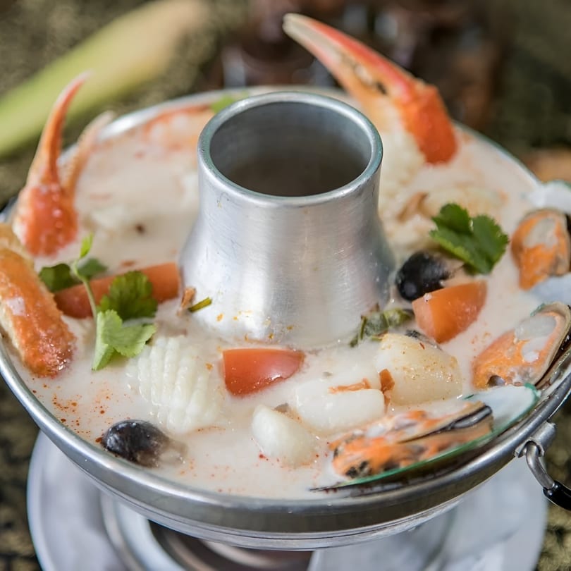 Thai Tom Yum soup with crab, mussels, squid, and vegetables in a metal hot pot.