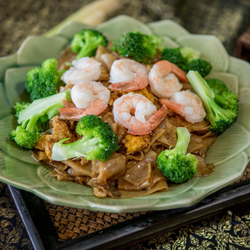 Thai Pad See Ew with shrimp and broccoli, served on a light green leaf-shaped plate.