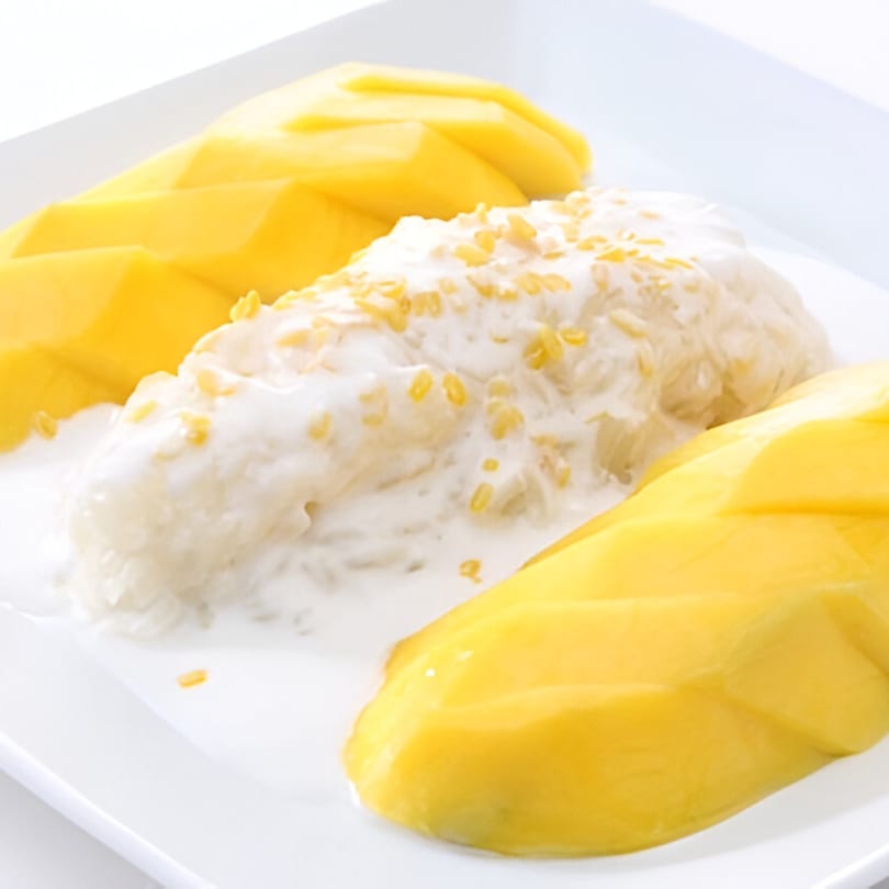 Thai mango sticky rice dessert with coconut milk and yellow mango slices on a white plate.