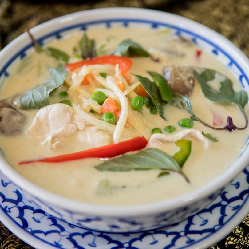 Close-up of a bowl of Thai green curry with chicken, bamboo shoots, peas, and red peppers.